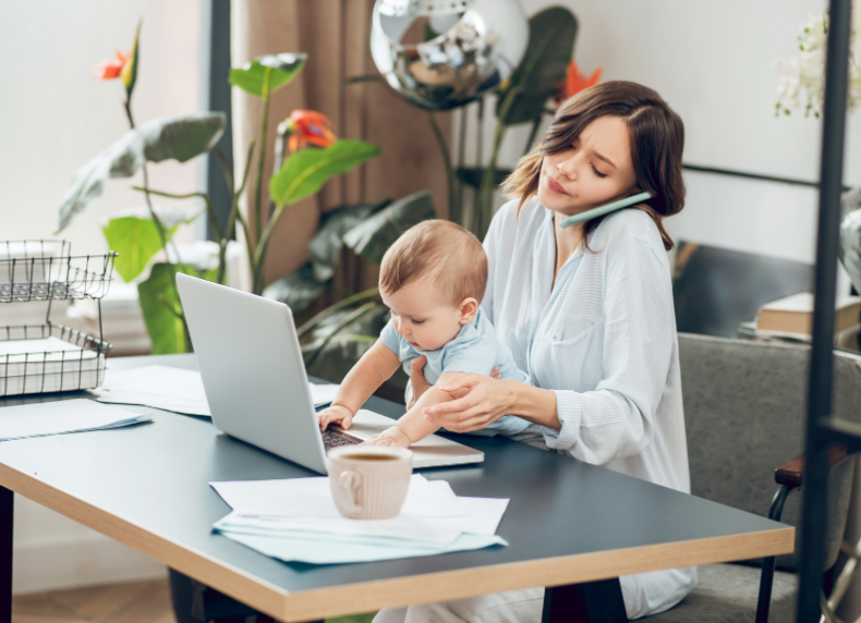 A working mother on a call while trying to work from home with her baby on her lap